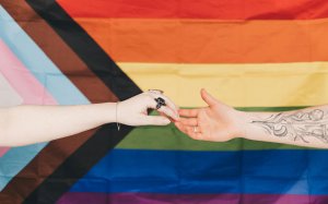 Hands touching with New Progress Pride Flag in background.